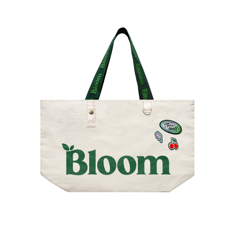 Beige tote bag with 'Bloom' branding on a light green background with decorative elements.